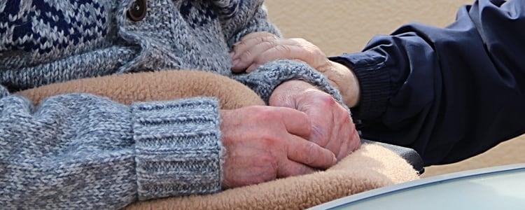 Eldre person med strikkegenser og teppe med hendene i fanget hodes i armen - Klikk for stort bilde